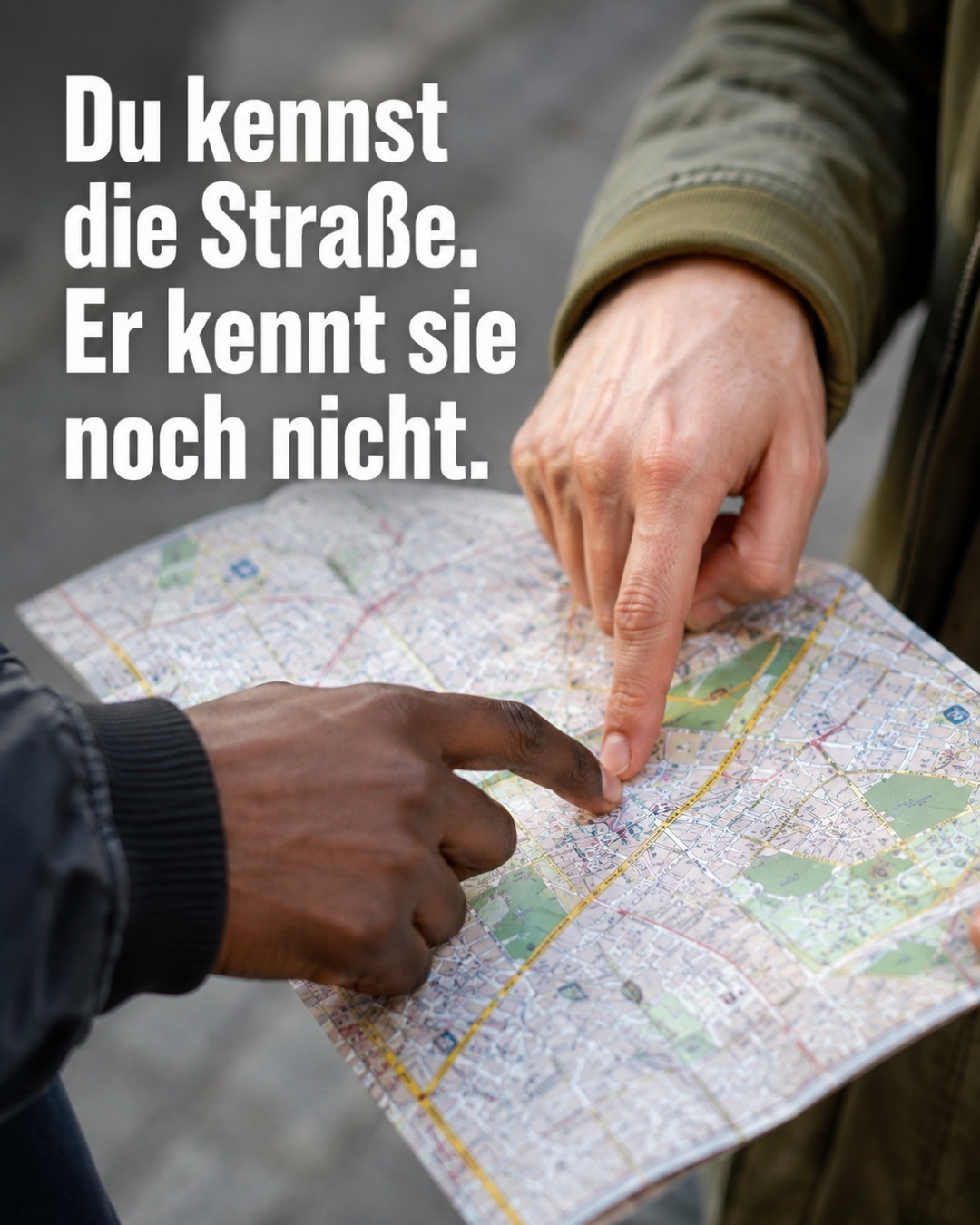 Zwei Personen mit unterschiedlicher Hautfarbe zeigen gemeinsam mit den Fingern auf einen Punkt einer aufgefalteten Stadtkarte. Darüber steht der Text: „Du kennst die Straße. Er kennt sie noch nicht."