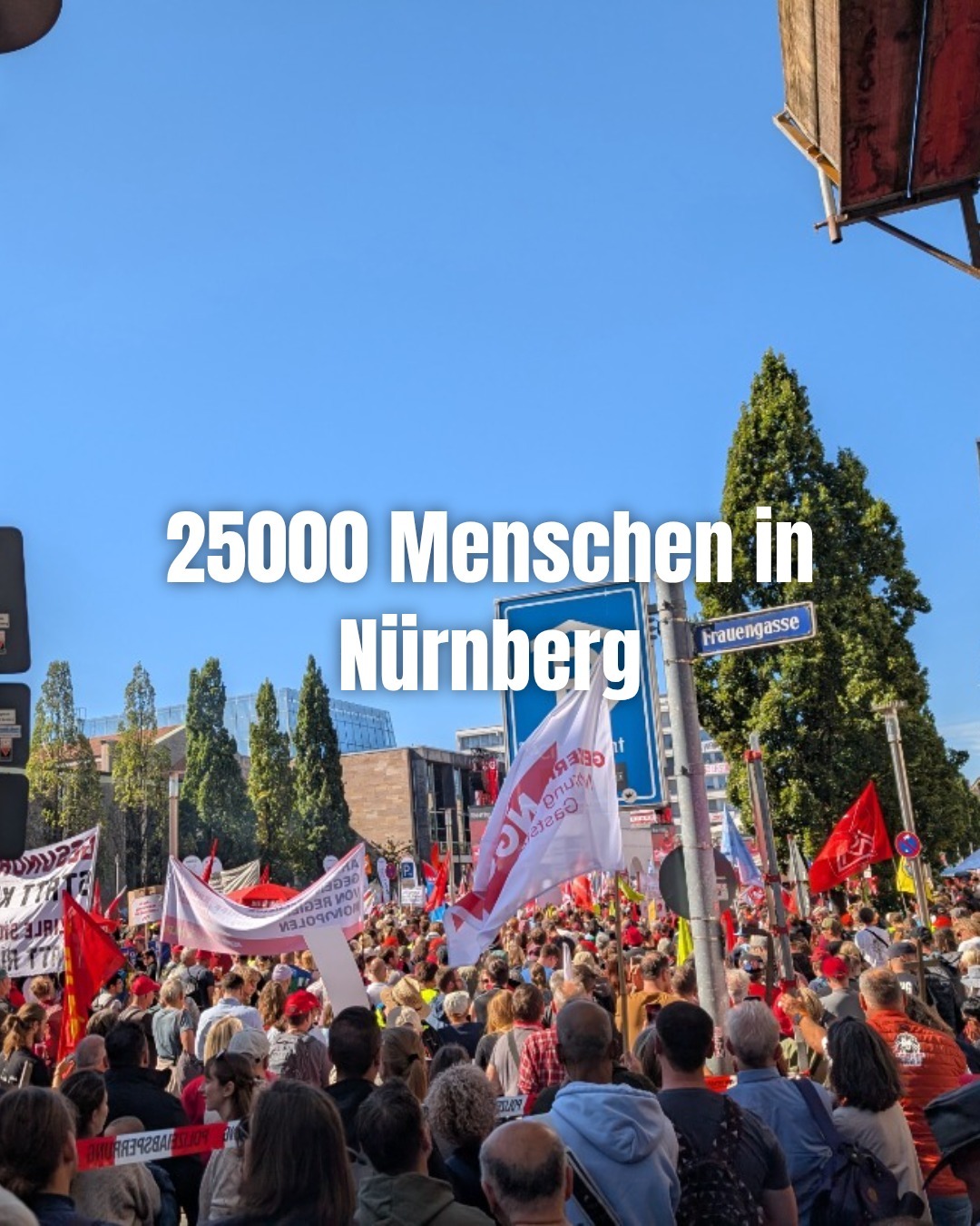 Große Menschenmenge bei einer Demonstration in einer Stadt mit zahlreichen roten Fahnen und Transparenten, unter anderem von Gewerkschaften, unter blauem Himmel an einer Straßenkreuzung mit dem Schild "Frauengasse". Über dem Bild steht der Text "25000 Menschen in Nürnberg".